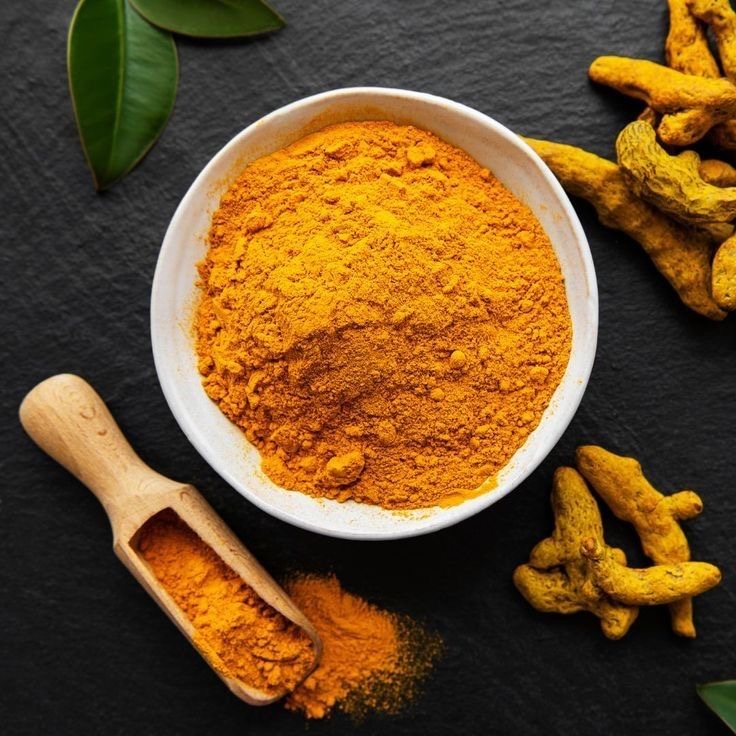 A bowl of golden turmeric powder beside fresh turmeric root