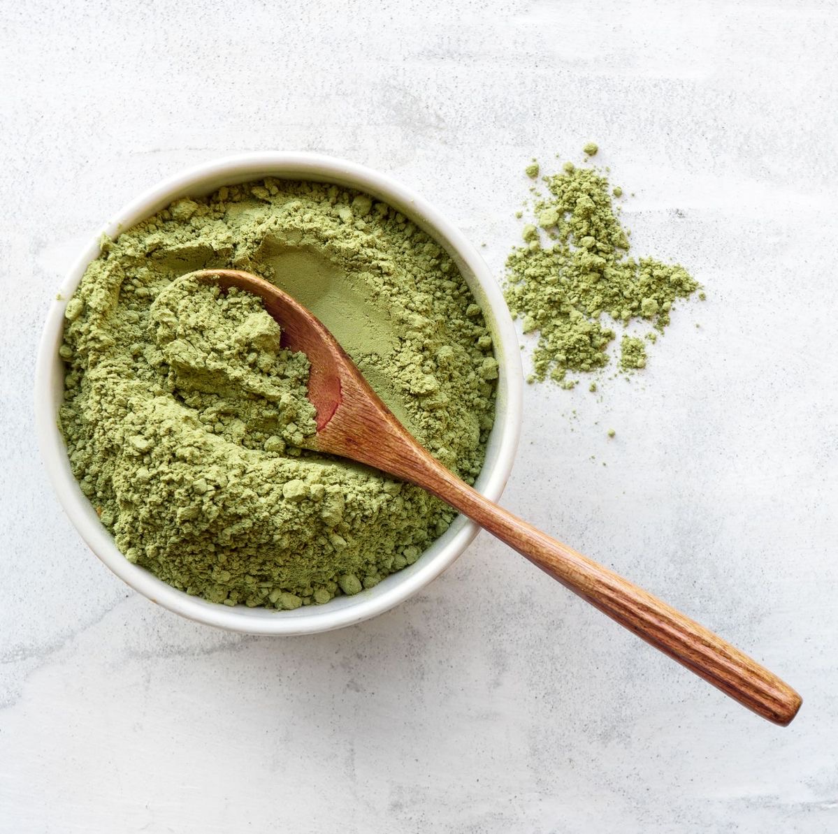 A bowl of vibrant green Qasil powder with a wooden spoon