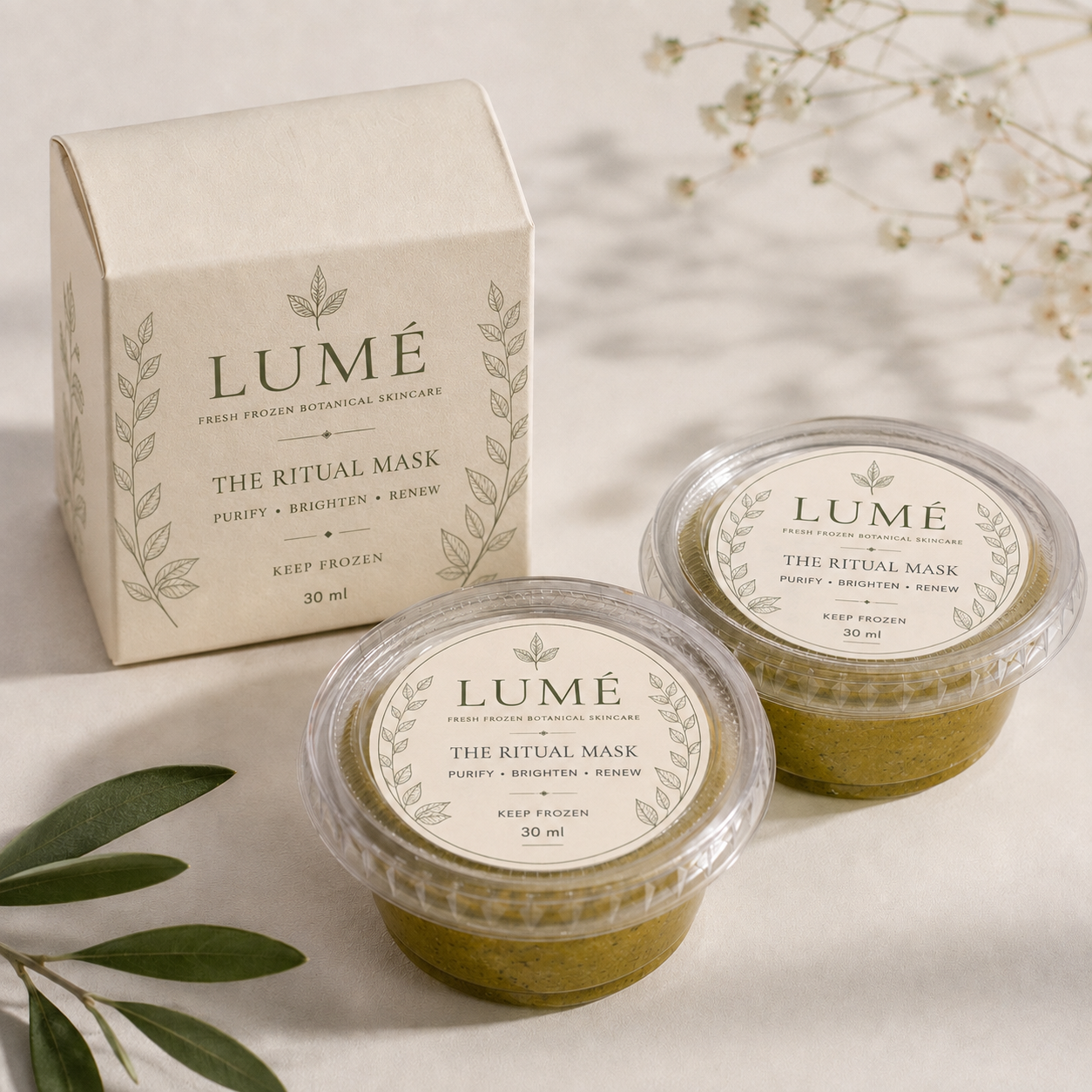 The official LUMÉ Ritual Mask carton with two Ritual Mask cups on warm ivory, olive leaves and gypsophila